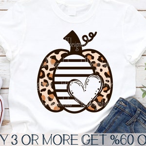 May include: A white t-shirt with a brown and black pumpkin design. The pumpkin has a heart in the center and is covered in a leopard print pattern. The text "BUY 3 OR MORE GET %60 OFF" is at the bottom of the image.