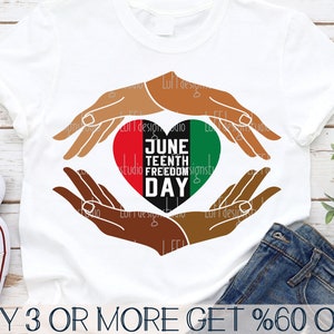 May include: A white t-shirt with a heart design featuring the words "Juneteenth Freedom Day" in black and red text. Two brown hands are forming a heart shape around the design.