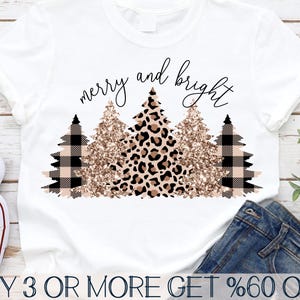 Könnte beinhalten: Weißes T-Shirt mit dem Text "merry and bright" in schwarzen Buchstaben. Das Design zeigt drei stilisierte Weihnachtsbäume mit Leopardenmuster, Glitzer und Karomuster.