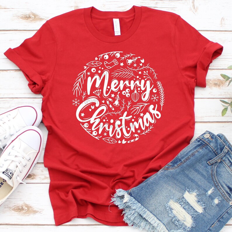 May include: Red t-shirt with a white graphic design of a circle with the words "Merry Christmas" and various Christmas-themed illustrations.