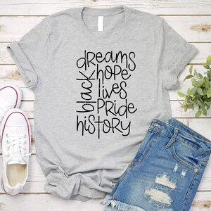 May include: A gray t-shirt with the text "dreams hope black lives pride history" printed in black.