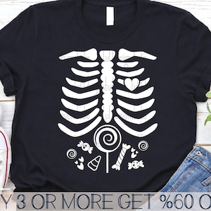 May include: Black t-shirt featuring a white skeleton design with candy graphics. The skeleton has a heart in its chest and is holding a lollipop. The text "BUY 3 OR MORE GET %60 OFF" is at the bottom of the image.