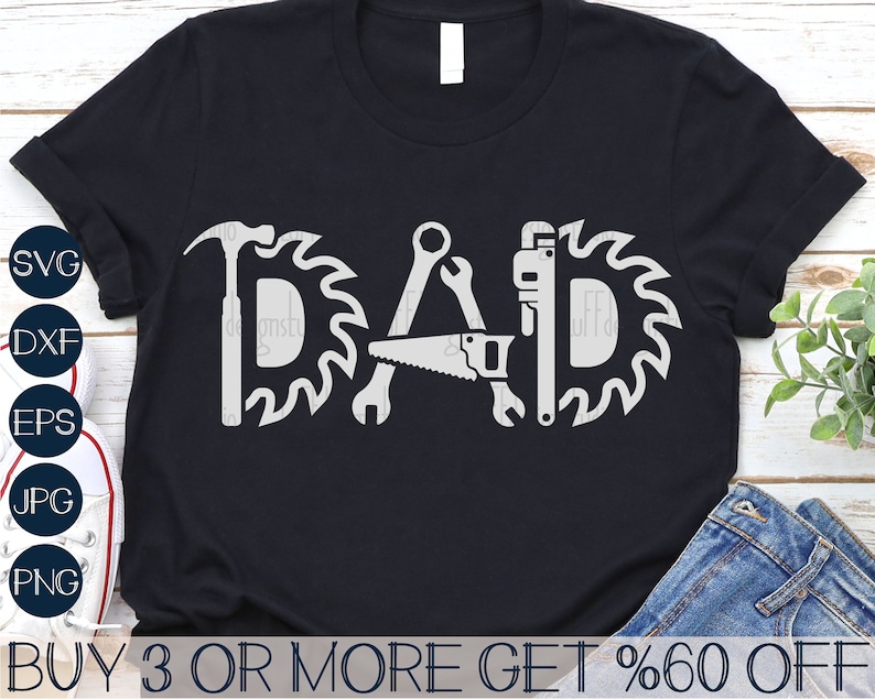 May include: A black t-shirt featuring a white graphic design of the word "DAD" formed from tools such as a hammer, saw, and wrench. The tools are encircled by saw blades.