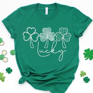 May include: A green t-shirt with a white design of three shamrocks and the word "lucky" on the front.