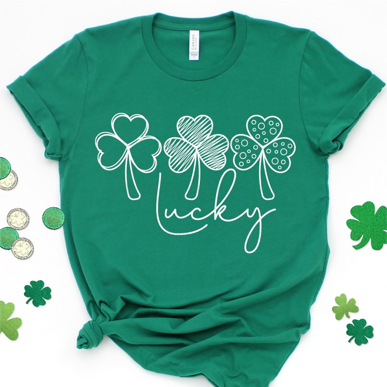May include: A green t-shirt with a white design of three shamrocks and the word "lucky" on the front.
