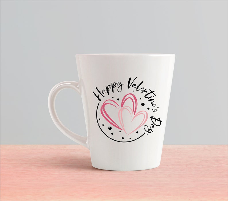 Puede incluir: Taza de cer&aacute;mica blanca con un dise&ntilde;o circular negro con el texto "Happy Valentine's Day" y dos corazones rosas.