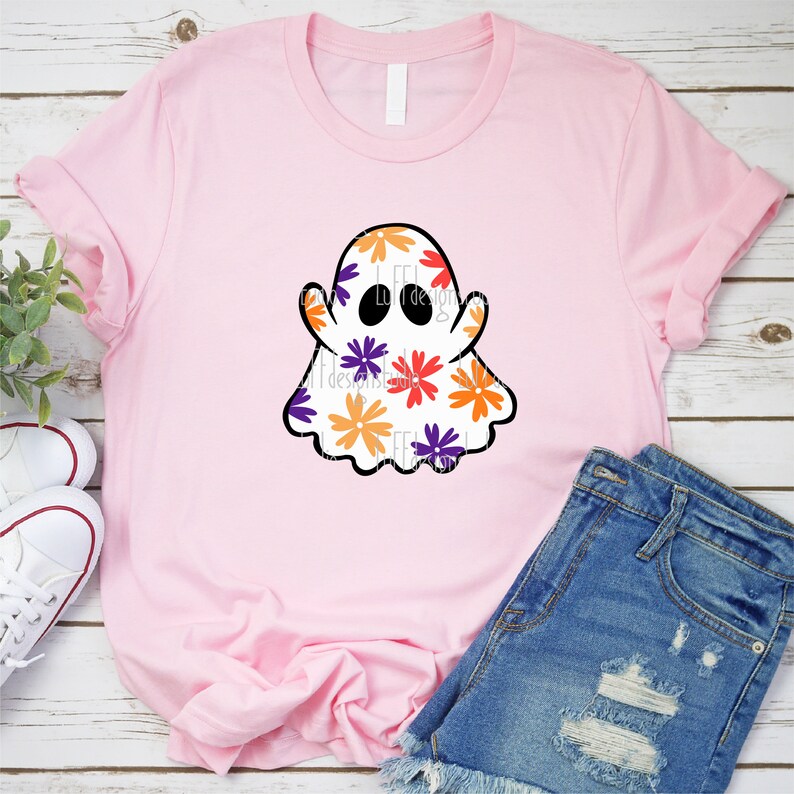 May include: A pink t-shirt with a white ghost design. The ghost is covered in a pattern of orange, purple, and yellow flowers.