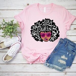 May include: Pink t-shirt with a black and white graphic of a woman with an afro. The graphic includes the words "Magic", "Love", "Queen", "Strong", and "Black".