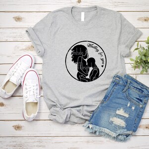 May include: A gray t-shirt with a black circle design featuring a silhouette of a pregnant woman holding a baby. The text "Waiting for you" is written inside the circle.