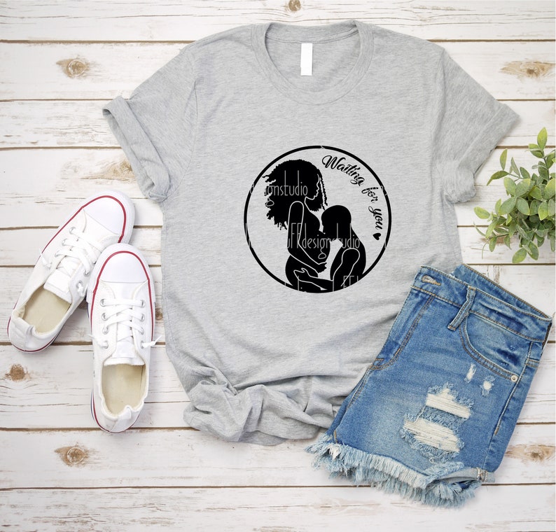 May include: A gray t-shirt with a black circle design featuring a silhouette of a pregnant woman holding a baby. The text "Waiting for you" is written inside the circle.