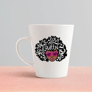 May include: White ceramic mug with a black and white graphic of a woman with an afro hairstyle. The graphic includes the words "Magic", "Strong", "Queen", "Love", and "Black". The woman is wearing pink sunglasses.