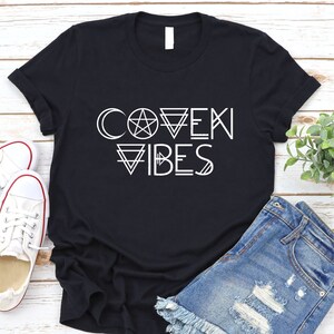 May include: Black t-shirt with white text that reads "Coven Vibes" with a pentagram and other geometric shapes.
