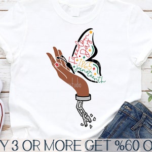 May include: A white t-shirt with a black hand holding a butterfly with the words "Freedom Day 1865 Juneteenth" written on it. The butterfly is red, green, yellow, and black. The hand is shackled with a chain.