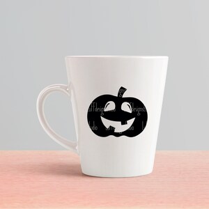 Op de afbeelding: Een witte keramische mok met een zwart silhouet van een jack-o'-lantern met een tandenrij.