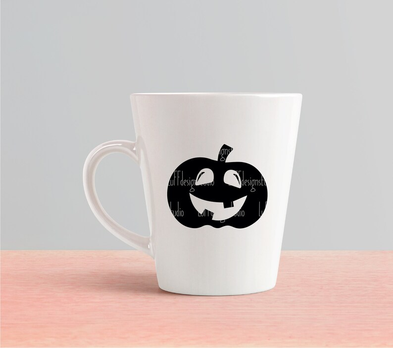 Op de afbeelding: Een witte keramische mok met een zwart silhouet van een jack-o'-lantern met een tandenrij.