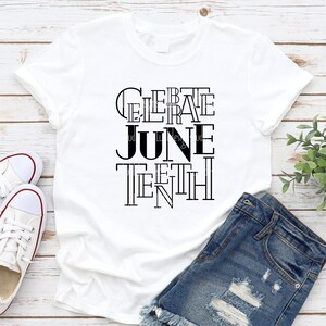 May include: White t-shirt with black text that reads "Celebrate Juneteenth". The text is in a stylized font with the letters stacked on top of each other.