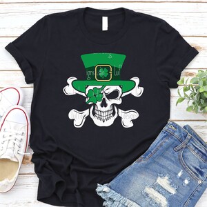 May include: Black t-shirt with a green leprechaun skull wearing a hat with a shamrock on it. The skull has a shamrock over one eye.