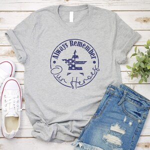 May include: A gray t-shirt with a blue circle design featuring a star with an American flag pattern and the text "Always Remember Our Heroes".