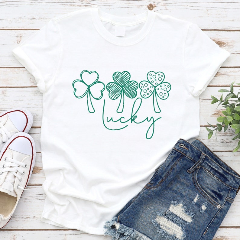May include: White t-shirt with a green outline of three shamrocks and the word "lucky" written in cursive.