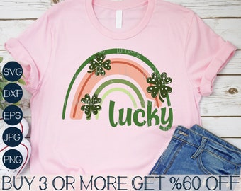 May include: A pink t-shirt with a green shamrock rainbow and the word "lucky" in green. The shirt is on a wooden surface with a pair of blue jeans.