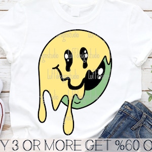 May include: A yellow and green smiley face graphic with dripping edges. The graphic is on a white t-shirt. The text "BUY 3 OR MORE GET %60 OFF" is at the bottom of the image.