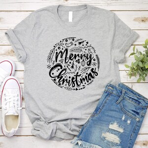 May include: A gray t-shirt with a black graphic design of a circle with the words "Merry Christmas" and various Christmas-themed illustrations.