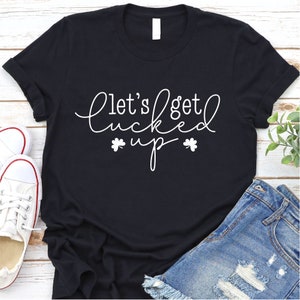 May include: Black t-shirt with white text that reads "Let's get lucked up" with shamrock symbols on either side of the word "up".
