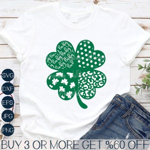 May include: A white t-shirt featuring a green four-leaf clover design. The clover is composed of four different patterns: polka dots, leopard print, small clovers, and the words "lucky" written in a cursive font. The text "BUY 3 OR MORE GET %60 OFF" is at the bottom of the image.