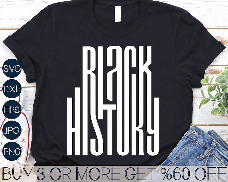 May include: Black t-shirt with white text that reads "Black History" in a bold, blocky font. The shirt is laying on a wooden surface with a pair of jeans and a pair of white sneakers.