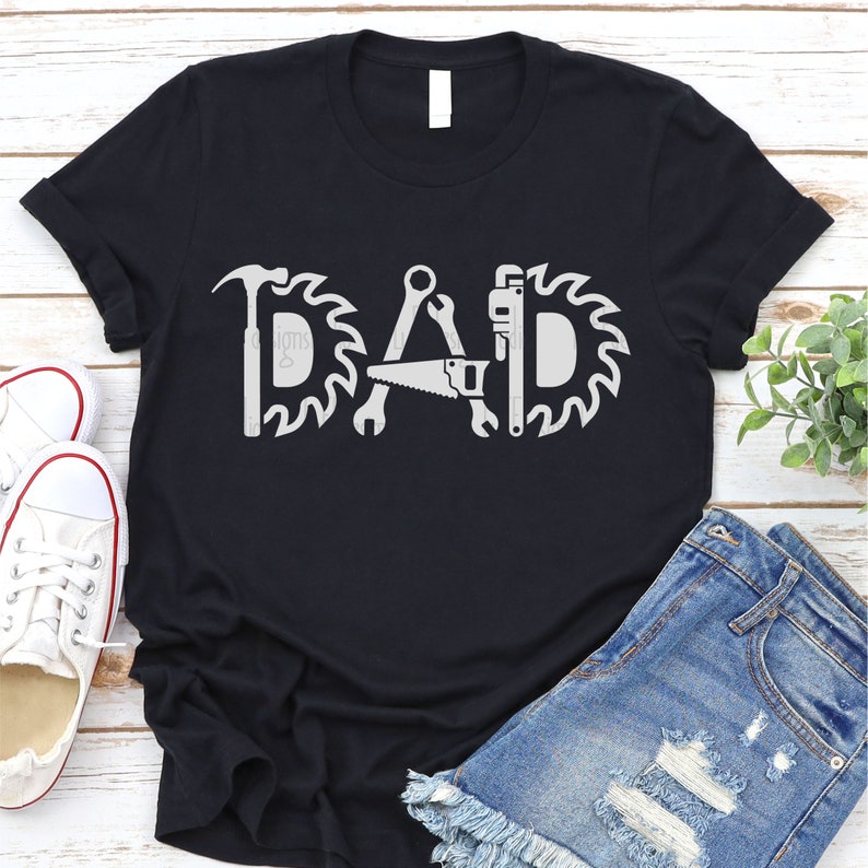May include: Black t-shirt with a white graphic of the word "DAD" made up of tools like a hammer, saw, wrench, and a saw blade.