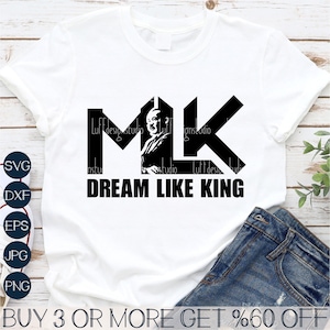 Peut inclure: Un t-shirt blanc avec un motif graphique noir des lettres "MK" avec une silhouette de Martin Luther King Jr. à l'intérieur des lettres. Le texte "DREAM LIKE KING" est sous les lettres.