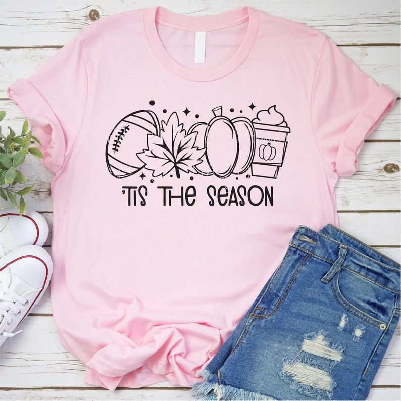 May include: A pink t-shirt with a black graphic of a football, a leaf, a pumpkin, and a coffee cup. The text "Tis the season" is below the graphic.