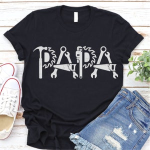 Peut inclure: T-shirt noir avec un motif blanc d'outils orthographiant le mot "PAPA".