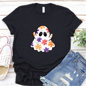 May include: A black t-shirt with a white ghost design. The ghost is covered in colorful flowers with orange, red, purple, and yellow accents.