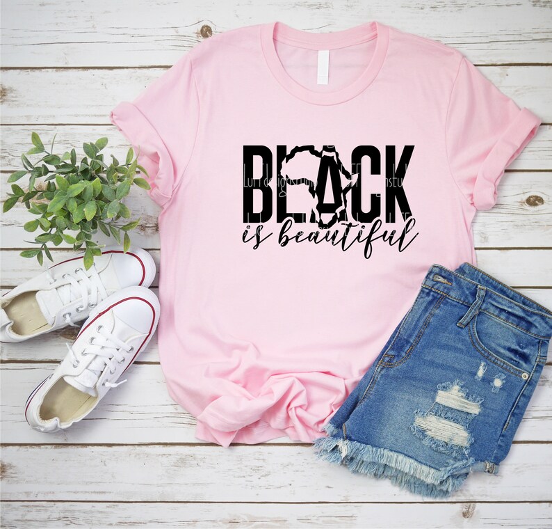 May include: Pink t-shirt with black text that reads "BLACK is beautiful". The text is styled with a silhouette of the continent of Africa.