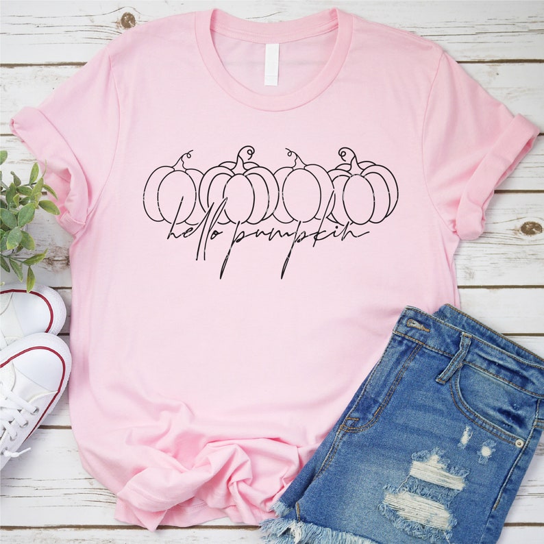 Pode incluir: Uma camiseta rosa com um gr&aacute;fico preto de quatro ab&oacute;boras e o texto "hello pumpkin".