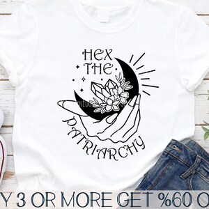 May include: Black and white graphic design of a hand holding a crescent moon with a crystal and flowers. The text "Hex the Patriarchy" is below the moon.