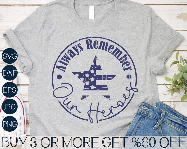 May include: A gray t-shirt with a blue circle design featuring a star with an American flag pattern. The text "Always Remember Our Heroes" is written around the star. The text "BUY 3 OR MORE GET %60 OFF" is written at the bottom of the image.