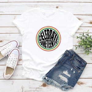 K&ouml;nnte beinhalten: Wei&szlig;es T-Shirt mit einem schwarzen Kreis-Motiv, auf dem in einer Retro-Schriftart "Celebrate Juneteenth" steht. Der Kreis ist von roten, gelben und gr&uuml;nen Streifen umgeben.