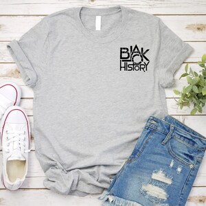 K&ouml;nnte beinhalten: Ein graues T-Shirt mit dem Aufdruck "Black History" in Schwarz auf der Vorderseite.