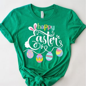 May include: Green t-shirt with a white graphic that says "Happy Easter" with bunny ears and colorful Easter eggs.