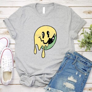 May include: A grey t-shirt with a yellow and green dripping smiley face graphic.