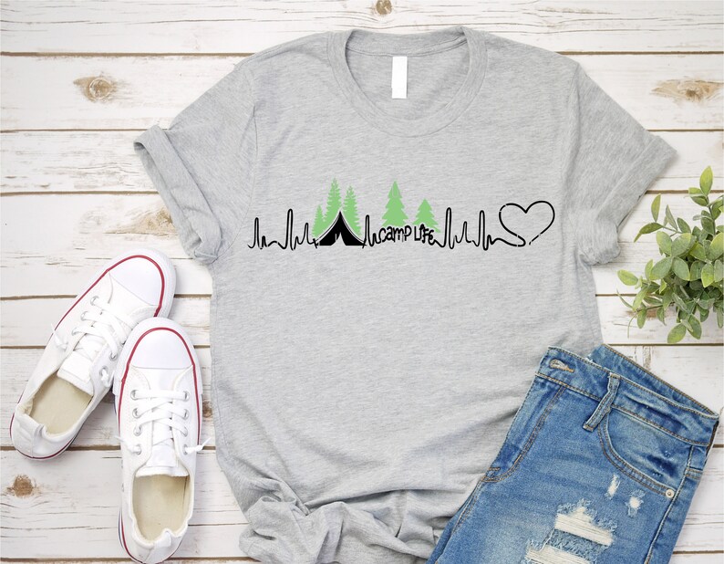 Op de afbeelding: Een grijs T-shirt met een zwart en groen ontwerp van een hartslag met een tent en bomen. De tekst "camp life" is in het ontwerp opgenomen.