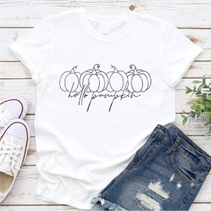 Pode incluir: Camiseta branca com um contorno preto de cinco ab&oacute;boras e o texto "hello pumpkin" em uma fonte cursiva.