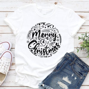 May include: White t-shirt with a black graphic design of a circle with the text "Merry Christmas" surrounded by holiday-themed illustrations.