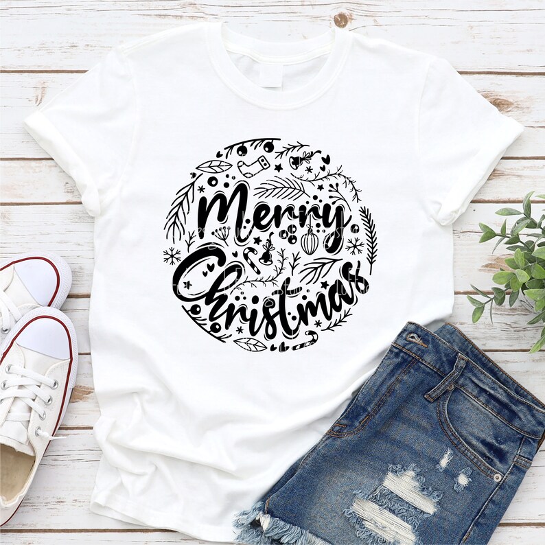May include: White t-shirt with a black graphic design of a circle with the text "Merry Christmas" surrounded by holiday-themed illustrations.