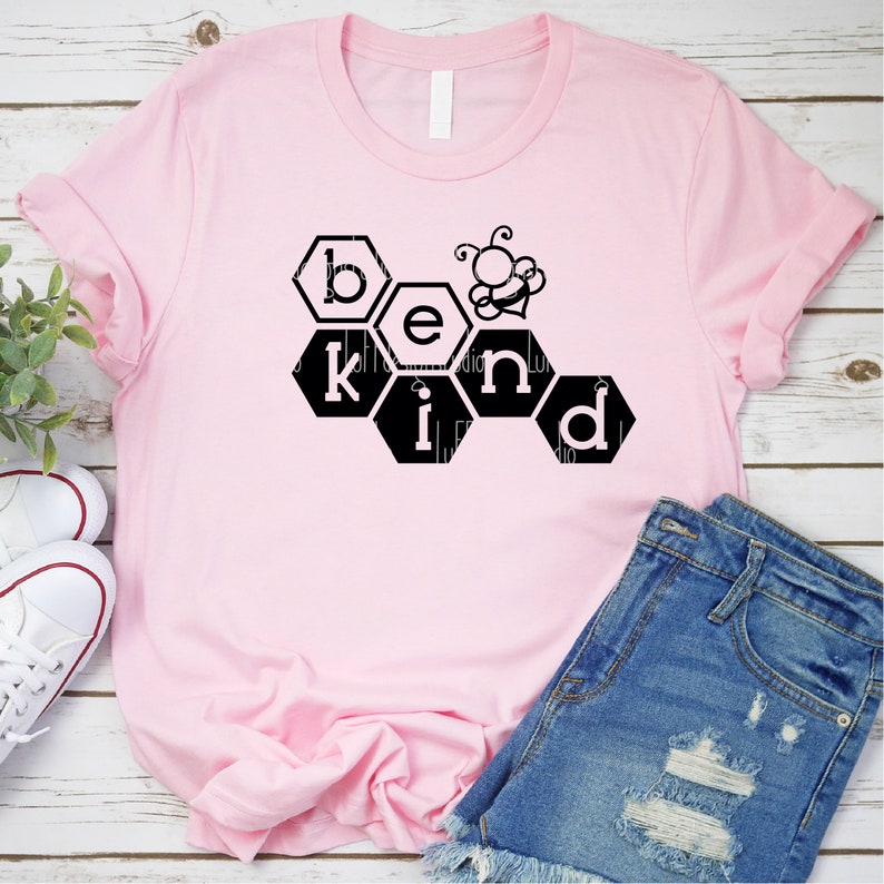 May include: Pink t-shirt featuring a black graphic of a honeycomb with the word "be kind" spelled out in the honeycomb cells. A small black bee is above the word "kind".