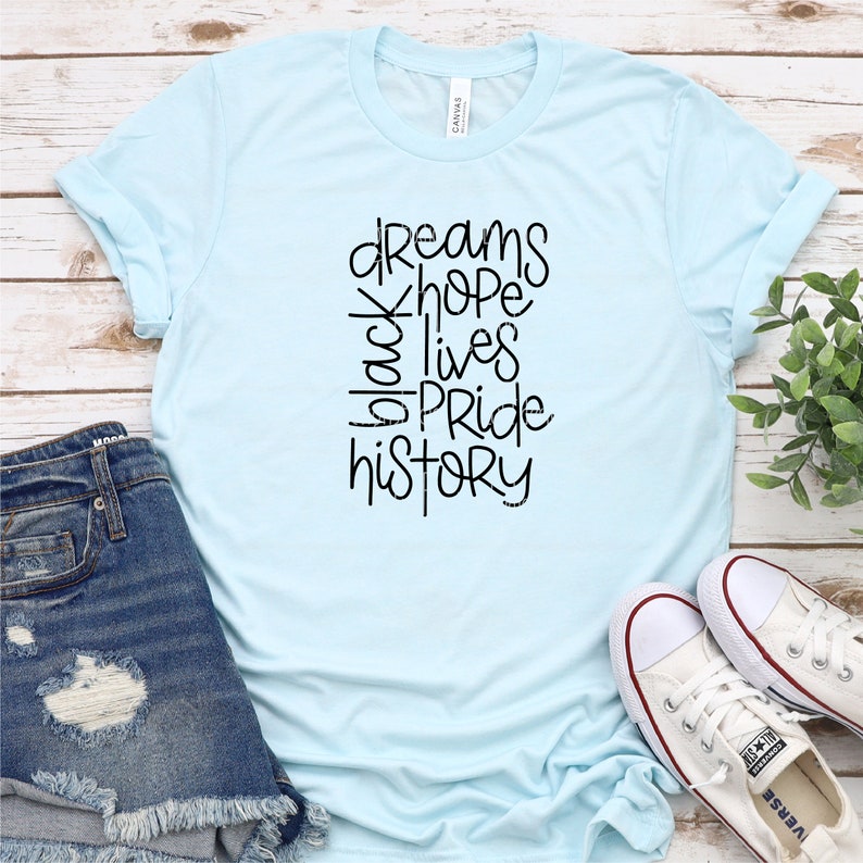 May include: A light blue t-shirt with black text that reads "dreams hope black lives pride history".