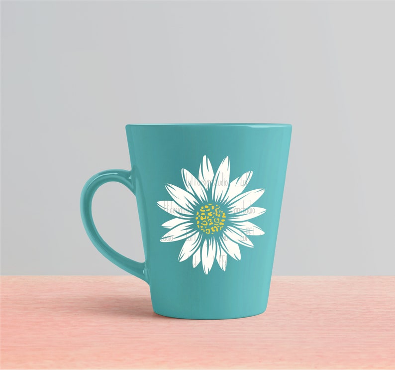 Op de afbeelding: Een teal keramische mok met een wit madeliefje ontwerp. De madeliefje heeft een gele kern met een luipaardprint.