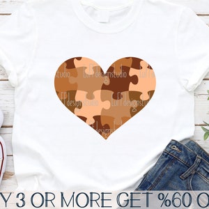 May include: A white t-shirt with a brown and orange puzzle piece heart design. The text "BUY 3 OR MORE GET %60 OFF" is at the bottom of the shirt.
